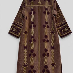 Pu&ograve; includere: Lungo cappotto in velluto marrone con ricami dorati e bordeaux. Il cappotto presenta motivi floreali e geometrici. Colletto alto e maniche a tre quarti.