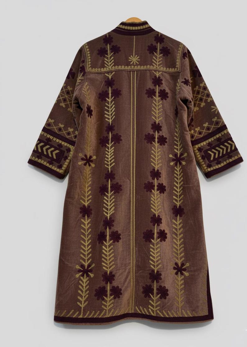 Pu&ograve; includere: Lungo cappotto in velluto marrone con ricami dorati e bordeaux. Il cappotto presenta motivi floreali e geometrici. Colletto alto e maniche a tre quarti.