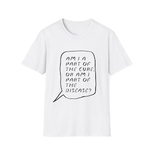 May include: White t-shirt featuring a black speech bubble with the text: "AM I PART OF THE CURE, OR AM I PART OF THE DISEASE?" The shirt has a crew neck and short sleeves.
