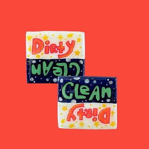Könnte beinhalten: Zwei rechteckige Schilder für Geschirr mit den Wörtern "Dirty" und "Clean" in farbenfrohen, verspielten Buchstaben. Die obere Hälfte ist weiß mit gelben Sternen, die untere Hälfte ist marineblau mit weißen Punkten. Der Hintergrund ist rot.