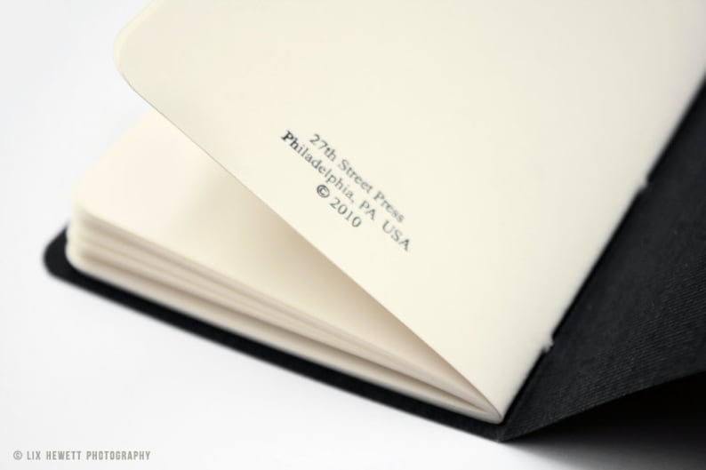 Może przedstawiać: Zbliżenie na wewnętrzną stronę okładki czarnego notesu. Papier jest biały, a tekst brzmi "27th Street Press, Philadelphia, PA USA &copy; 2010".