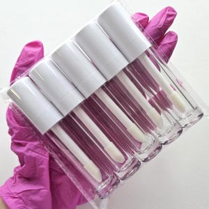 May include: A package of six clear lip gloss tubes with white caps and applicators. The tubes are filled with a mauve-colored gloss. The items are packaged in a clear plastic sleeve.