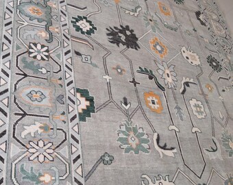 May include: A large, rectangular area rug with a light gray background and an intricate floral pattern in shades of green, black, white, and orange. The rug has a detailed border with geometric shapes and floral motifs.
