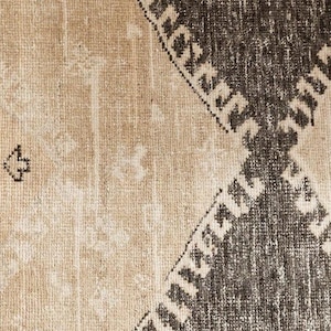 May include: A woven textile rug featuring a high-contrast geometric pattern. The design consists of large, dark charcoal grey diamond shapes set against a light beige background. The surface has a visible, textured weave with a distressed finish.
