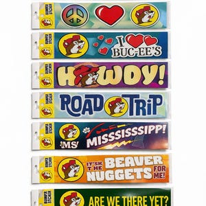 May include: A collection of bumper stickers with various designs and text. The stickers feature a cartoon beaver mascot and phrases like "I Brake for Buc-ee's," "Road Trip," and "Are We There Yet?" The color palette includes red, yellow, blue, and green.