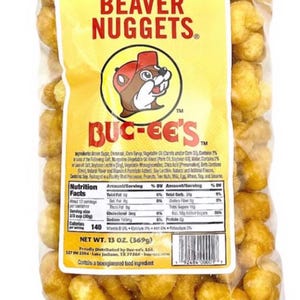 May include: A clear plastic bag filled with golden-brown Beaver Nuggets. The bag features a yellow label with the text "BEAVER NUGGETS" and the Buc-ee's logo. The net weight is 13 oz (369g).