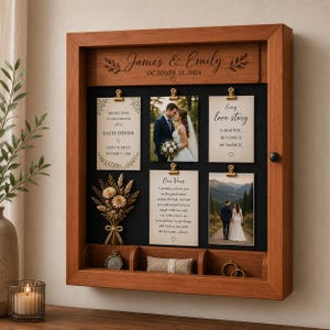 May include: A wooden shadow box display case with a dark interior, featuring a personalized header reading James & Emily October 12, 2024. It holds four photos, two text cards, a dried floral bouquet, a small clock, a ring pillow, and two gold rings.