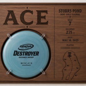 May include: A square wooden plaque featuring a light blue Innova Destroyer disc golf disc mounted in the center. The plaque is engraved with ACE, Storrs Pond Disc Golf Course, Hole 7, 215 ft, May 18, 2025, and a diagram of the course hole layout.