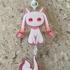 May include: A white and pink anime-style keychain featuring a cat-like character with pink eyes and ears, gold armbands, and a tail. The keychain has a heart-shaped clasp and a chain.