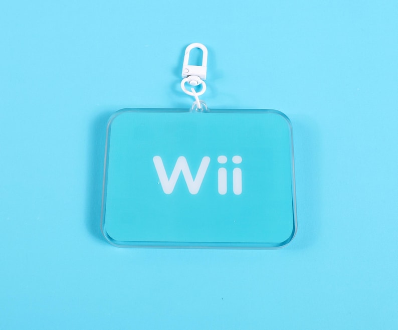 May include: A clear, rectangular keychain with rounded corners and a white metal clasp. The keychain has a light blue background with the word "Wii" printed in white.