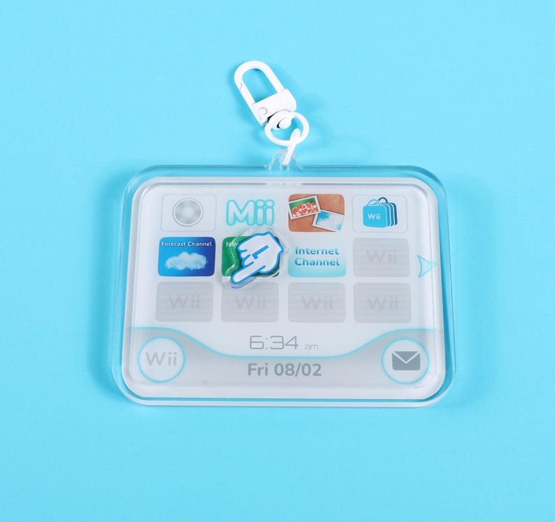 May include: A clear, rectangular keychain featuring a Wii interface design. The keychain has a white border and includes icons for Forecast Channel, Internet Channel, and more. The time displayed is 6:34 am, and the date is Fri 08/02.