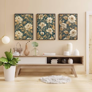 May include: Three framed floral art prints. Each print features a dark teal background with cream and gold-colored roses and foliage. The frames are black. The prints are displayed above a wooden console table.