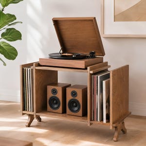 May include: A wooden record player console featuring a top-mounted turntable with a black platter and tonearm. The unit includes two side storage compartments filled with vinyl records and a central shelf housing two matching wooden speakers.