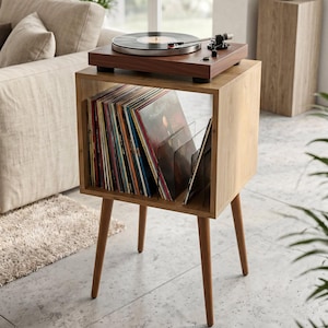 Puede incluir: Una mesa auxiliar de madera de color marrón claro con cuatro patas cónicas y un compartimento de almacenamiento cuadrado abierto lleno de una colección de discos de vinilo. Un tocadiscos de madera oscura descansa sobre la mesa.