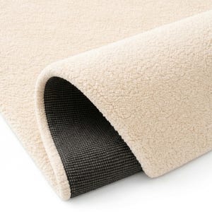 A close-up detail shot of a cream hand-tufted rug showing the soft, dense wool pile and the durable, non-slip grey canvas backing for enhanced floor protection and safety.