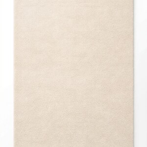 A studio product shot of a rectangular, cream-colored hand-tufted rug with a soft, plush texture and uniform pile, isolated against a clean white background.