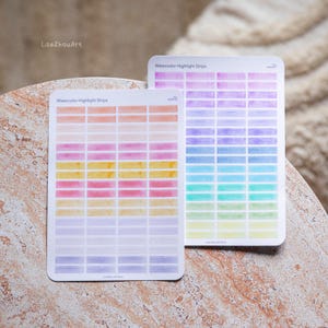 Könnte beinhalten: Zwei Stickerbögen mit Aquarell-Highlight-Streifen. Die Bögen zeigen Reihen rechteckiger Blöcke in einem Farbverlauf, darunter Orange, Rosa, Gelb, Grün, Blau und Lila. Der Text "Watercolor Highlight Strips" ist auf jedem Bogen aufgedruckt.