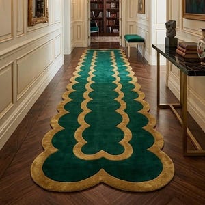 May include: A long runner rug featuring a scalloped edge design in deep emerald green and gold. The rug is positioned in a hallway with cream-colored paneled walls, a crystal chandelier, wall sconces, a console table, and a library room.