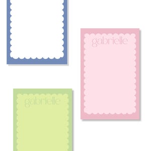 May include: Three personalized notepads in pastel colors: blue, pink, and green. Each notepad has a scalloped border and the name "gabrielle" printed at the top. The notepads are rectangular and have a clean, minimalist design.