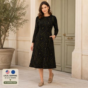 Puede incluir: Un vestido midi negro de manga larga con cuello redondo y un estampado floral en líneas doradas. El vestido presenta un cuerpo ajustado, una falda acampanada y bolsillos laterales visibles, combinado con zapatos planos de color beige.