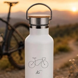 Op de afbeelding: Witte waterfles met een zwarte fietsillustratie en de naam "Noah" in script. De fles heeft een houten deksel, een zilveren handvat en een zilveren band. Een fiets is zichtbaar op de achtergrond.