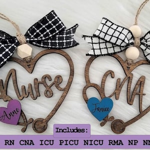 May include: Two wooden heart-shaped ornaments with a stethoscope design. The ornaments are decorated with black and white checkered ribbon and wooden beads. The text "Nurse" and "CNA" are written on the ornaments. The text "Anne" and "Janice" are written on smaller hearts attached to the ornaments.