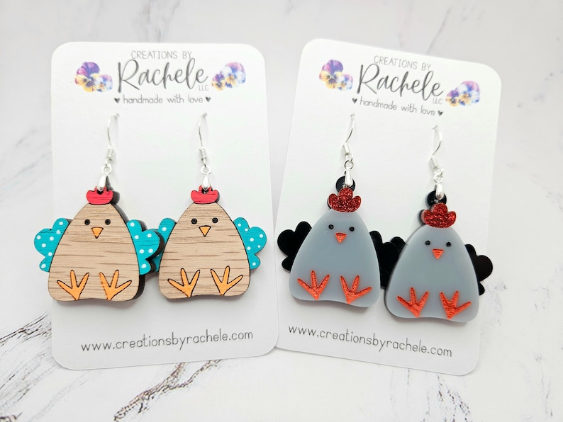 May include: Two pairs of chicken-shaped earrings. One pair is made of wood with turquoise and white accents, the other pair is made of gray acrylic with red accents. Both pairs have red glitter on the top of the chicken's head.