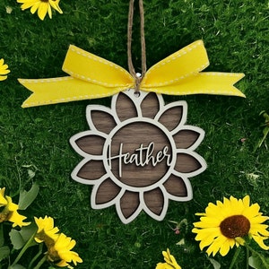 Może przedstawiać: Drewniana ozdoba w kształcie słonecznika z imieniem "Heather" napisanym kursywą w środku. Ozdoba jest ozdobiona żółtą wstążką.
