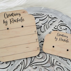 Op de afbeelding: Twee houten oorbellenstandaards met de tekst "Creations by Rachele" op elk. De grotere standaard heeft drie rijen gaten voor oorbellen en metingen in inches.