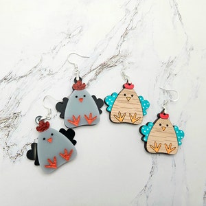 May include: Three pairs of chicken earrings. One pair is gray with red accents, another is brown with blue accents, and the last pair is brown with turquoise accents.