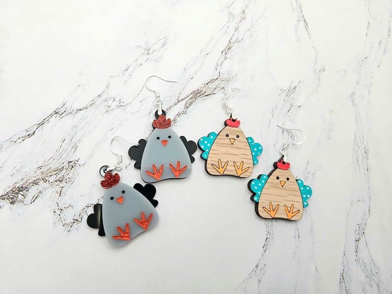 May include: Three pairs of chicken earrings. One pair is gray with red accents, another is brown with blue accents, and the last pair is brown with turquoise accents.