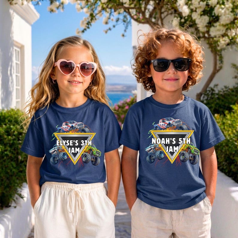 May include: Two children wearing navy blue t-shirts with a monster truck graphic. The shirts feature a yellow triangle with the text "ELYSE'S 3TH JAM" and "NOAH'S 5TH JAM" respectively, along with colourful monster truck illustrations.