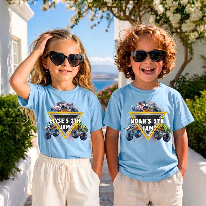 May include: Two children wearing light blue t-shirts with a monster truck graphic. The shirts have text that reads "ELYSE'S 3TH JAM" and "NOAH'S 5TH JAM". The children are wearing sunglasses and standing outdoors.