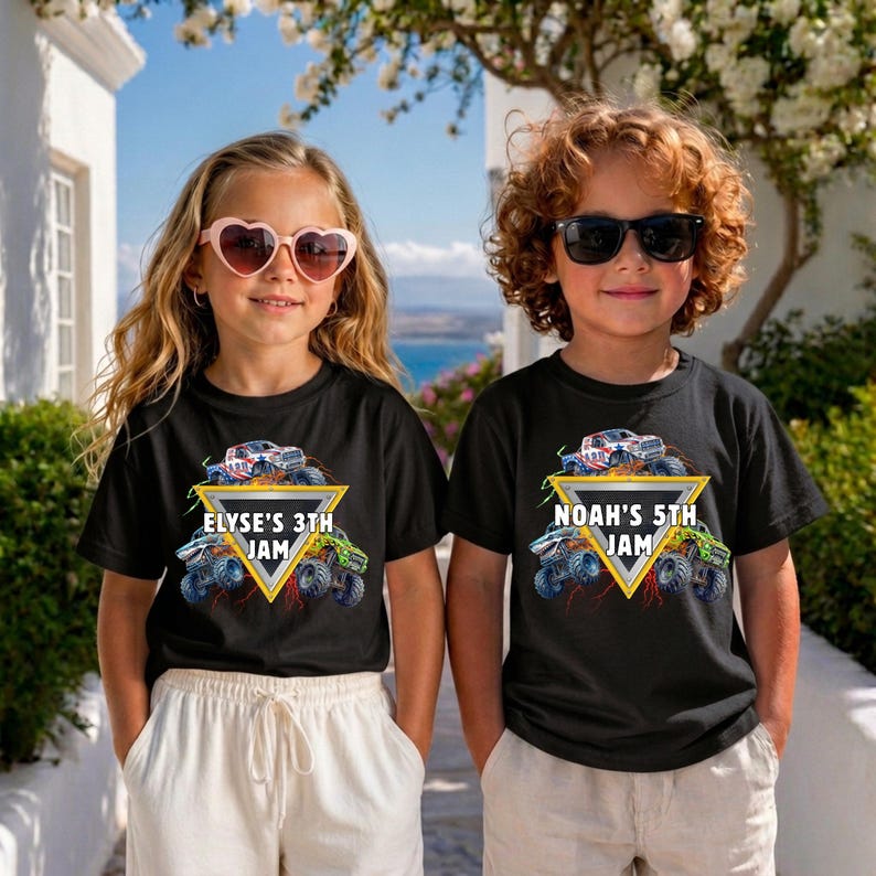May include: Two children wearing black t-shirts featuring a monster truck design. The shirts display the text "ELYSE'S 3TH JAM" and "NOAH'S 5TH JAM" within a yellow triangle. The background shows a blue sea and white buildings.
