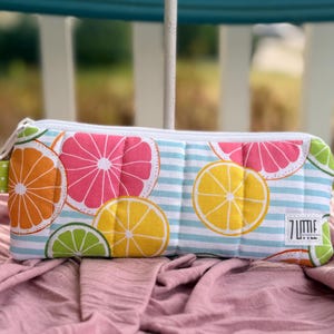 May include: A rectangular pencil case with a zipper closure. The case features a colorful pattern of citrus fruit slices, including oranges, grapefruits, lemons, and limes, set against a blue and white striped background. The text "7 Little" is visible.