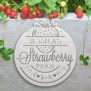 May include: A white metal sign with a strawberry design and the text "Jessica's Strawberry Patch picked fresh daily".