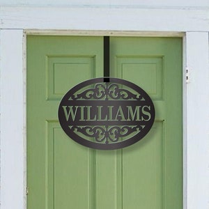 May include: Black metal oval door hanger with a decorative scroll design and the name "WILLIAMS" in white lettering.
