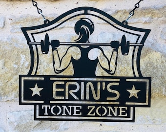 May include: Black metal sign with a silhouette of a person lifting weights. The sign reads "Erin's Tone Zone" with a star on each side of the name.