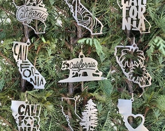 May include: Ten metal ornaments featuring a California theme. Each ornament is a different design, including a bear, palm tree, and a heart. The ornaments are all silver in color.