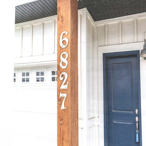 May include: A white wooden house with a blue door and the house number 6827 displayed on a brown wooden post.
