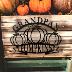 May include: Black metal sign with the words "Grandpa's Pumpkins" in a decorative font. The sign features a silhouette of five pumpkins with leaves and stems.
