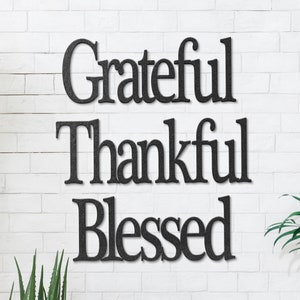 May include: Black wooden wall decor with the words "Grateful Thankful Blessed" in a serif font.