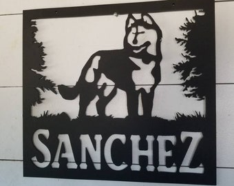 May include: Black metal sign with a silhouette of a husky dog standing in a forest. The name "SANCHEZ" is cut out below the dog.