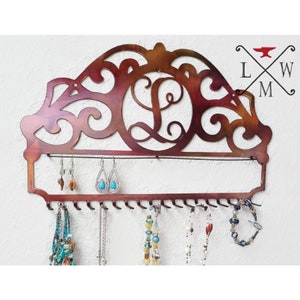 K&ouml;nnte beinhalten: Ein Schmuckorganizer aus Metall mit einem dekorativen Schn&ouml;rkeldesign und einem personalisierten Initial "L". Der Organizer hat Haken f&uuml;r Halsketten und Ohrringe und ein Regal f&uuml;r Armb&auml;nder.