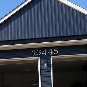 Pu&ograve; includere: Una casa blu con finiture bianche e un portone del garage. Il numero civico 13445 &egrave; visualizzato sulla facciata della casa.