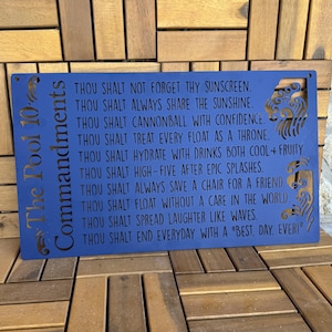 May include: Blue metal sign with the text "The Pool 10 Commandments" and a list of rules for poolside behavior. The sign features a wave design.