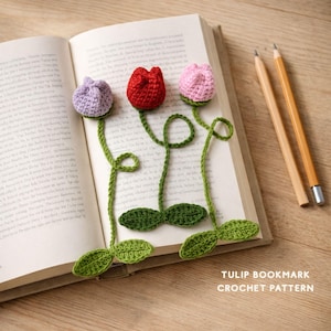 Può includere: Segnalibri a forma di tulipano all'uncinetto in viola, rosso e rosa, con steli e foglie verdi, appoggiati su un libro aperto. Due matite sono accanto al libro. Il testo "TULIP BOOKMARK CROCHET PATTERN" è visibile.