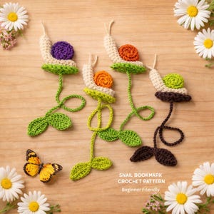 May include: Crocheted snail bookmarks in various colors, including purple, orange, and green, with cream-colored bodies and green leaves. The bookmarks are arranged on a wooden surface with daisies and a butterfly. Text on the image reads "Snail Bookmark Crochet Pattern Beginner Friendly."