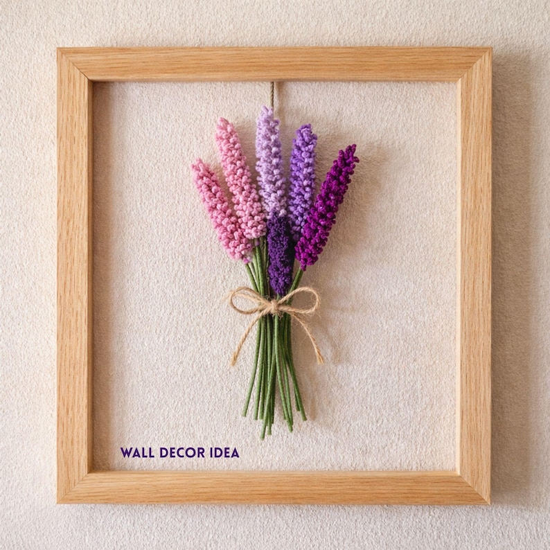 Op de afbeelding: Een ingelijste wanddecoratie met een boeket lavendelbloemen in roze, paarse en violette tinten. De bloemen zijn vastgebonden met touw en geplaatst tegen een neutrale achtergrond. De houten lijst geeft een rustieke uitstraling. Tekst linksonder: WALL DECOR IDEA.