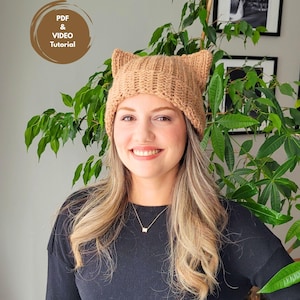 May include: A tan knitted cat ear hat. The hat is worn by a person with long blonde hair and a black shirt. The image also includes the text "PDF & VIDEO Tutorial" in a brown circle.